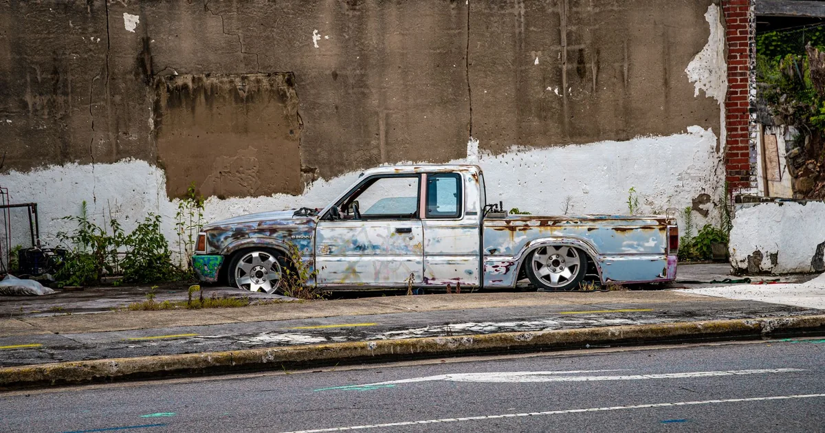 Abandoned truck parked against a weathered wall with overgrown.