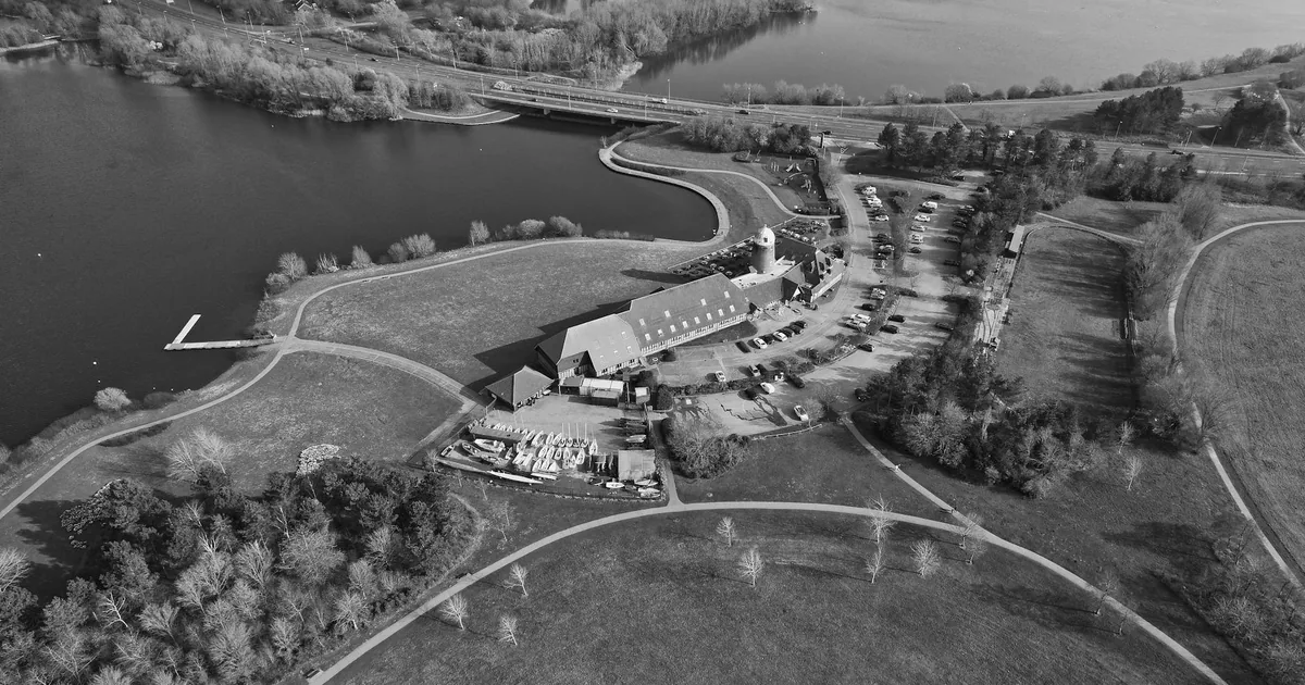 Aerial view of a parking area near a lake with trees and a building.