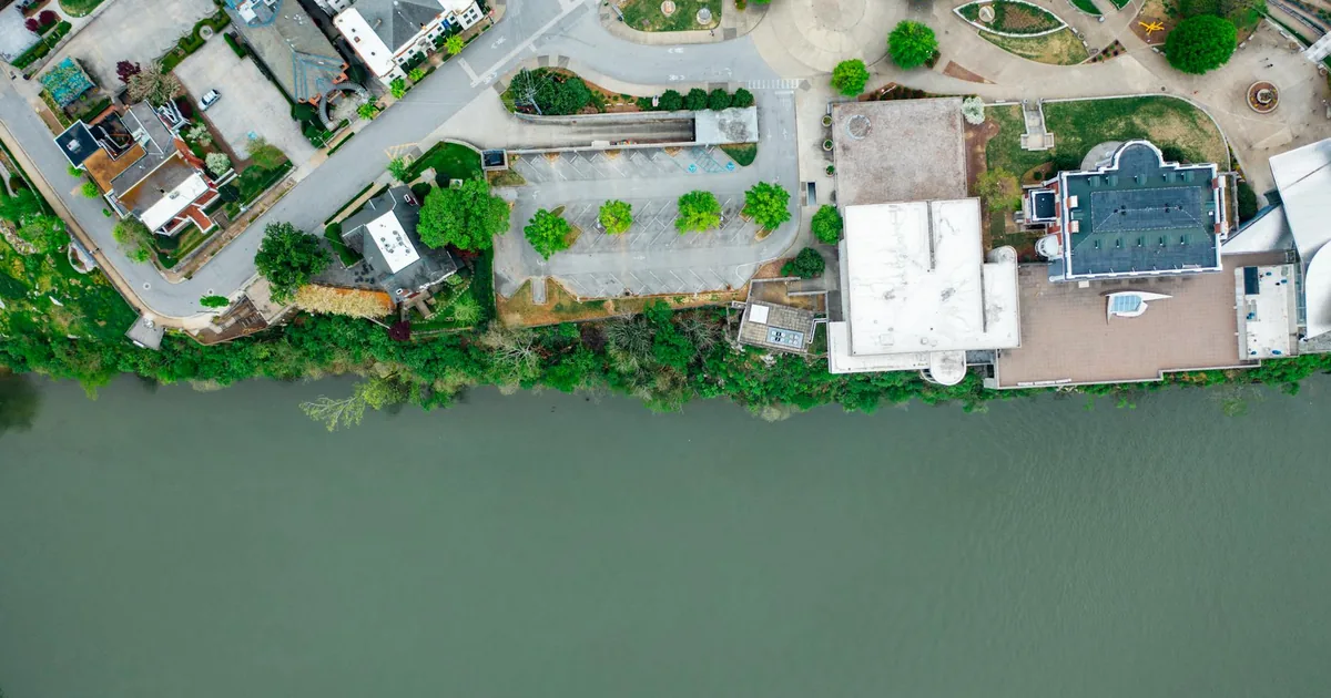 Aerial view of a parking area near buildings and a riverbank.