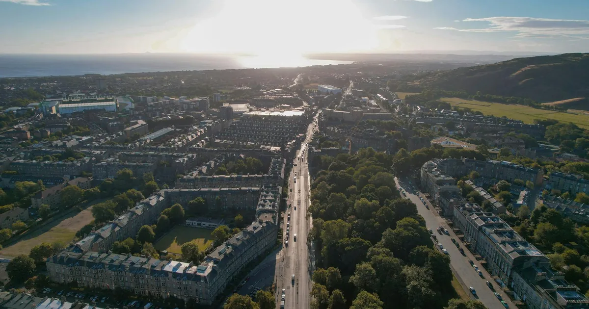Aerial view of a parking area with cars along tree lined streets.