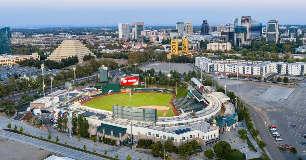 Aerial view of a parking lot near a stadium with city skyline in.