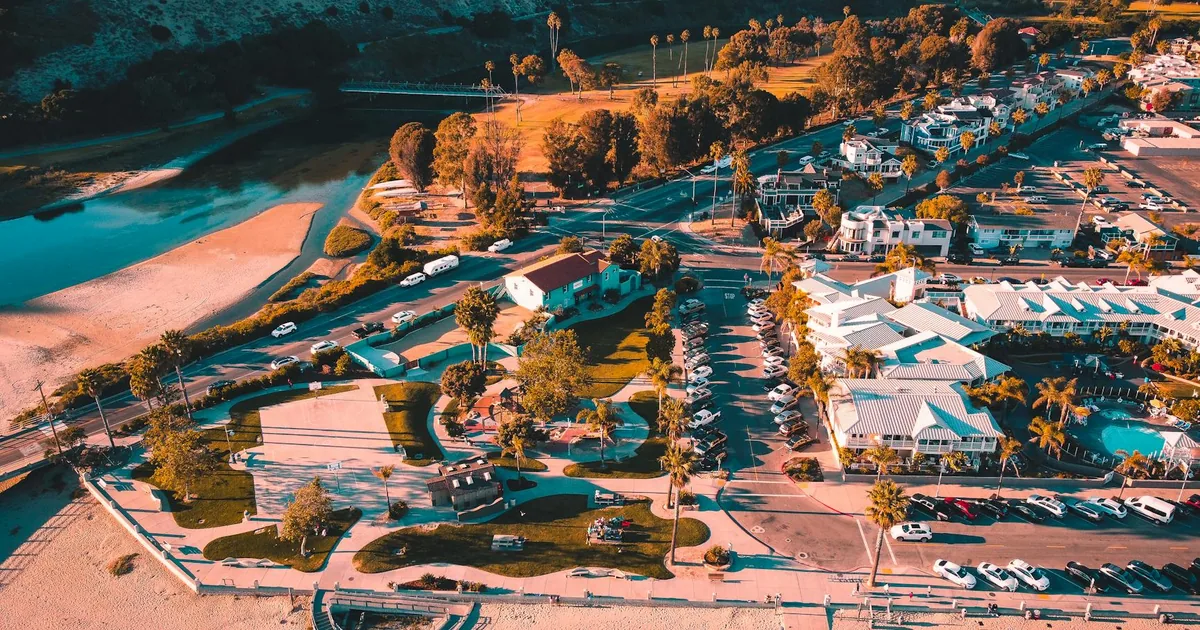 Aerial view of a parking lot with cars trees and nearby buildings.