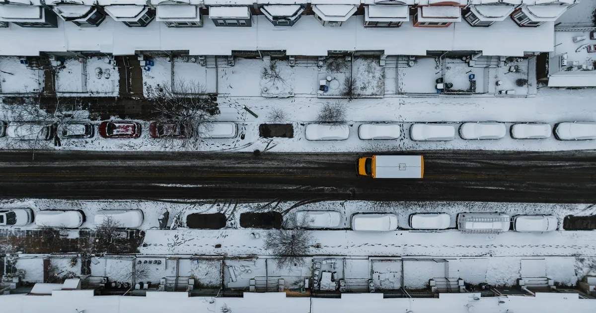 Aerial view of a snowy street with parked cars and residential.