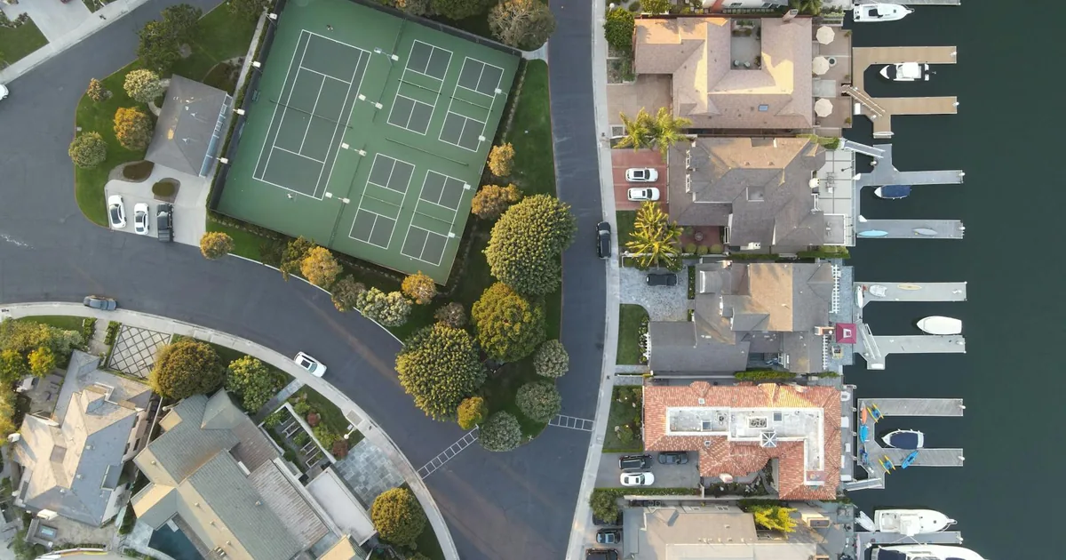 Aerial view of homes tennis courts and parked cars in a residential.