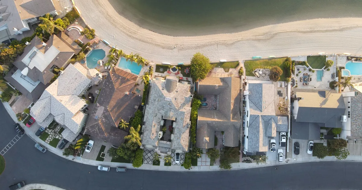 Aerial view of homes with parked cars along a waterfront street.