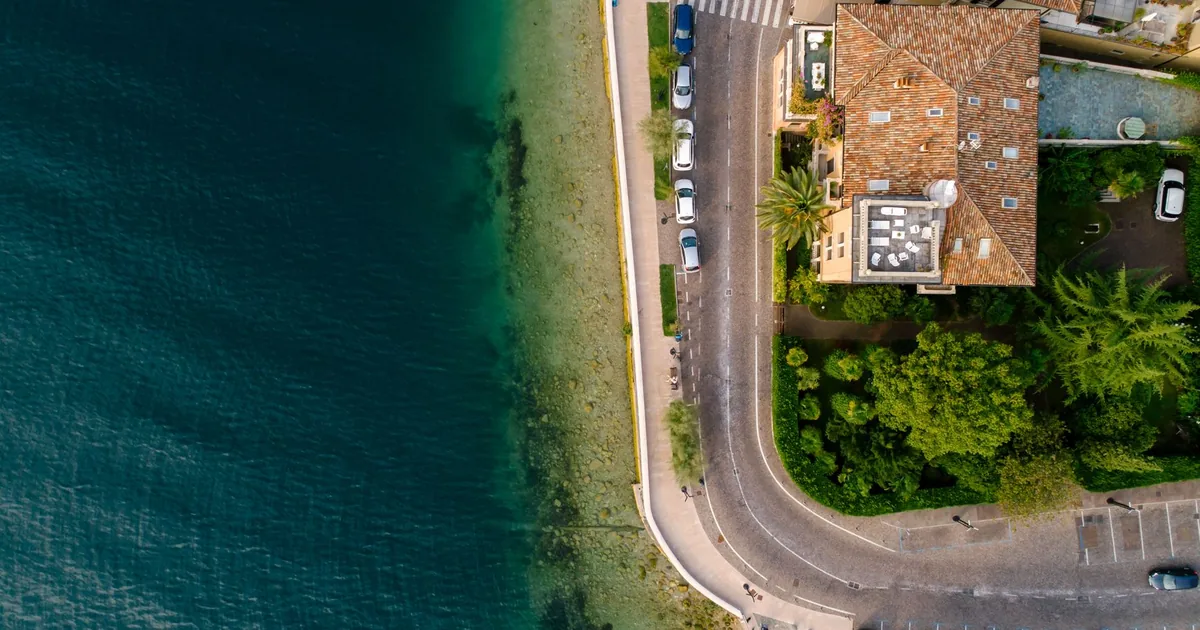 Aerial view of parked cars along a curved road by the water s edge.