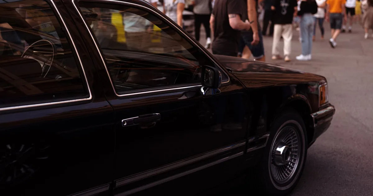 Black car parked near a crowd of people walking in a busy urban area.