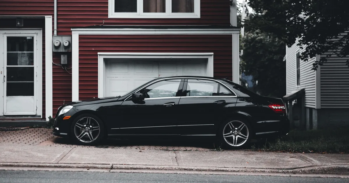 Black sedan parked on the curb next to a residential building.