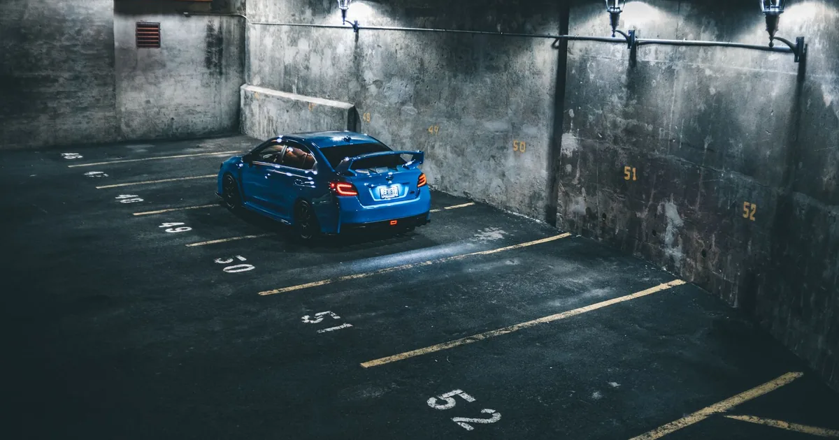 Blue car parked in a dimly lit parking garage with marked spaces.