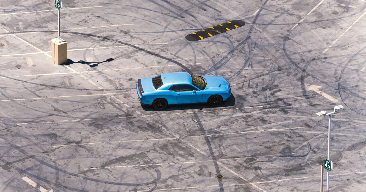 Blue car parked in an empty lot with tire marks on the pavement.