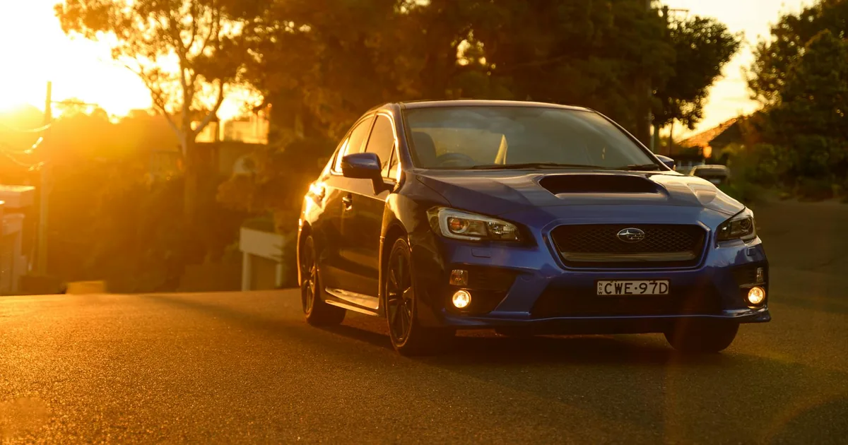 Blue car parked on a road during sunset with trees in the background.