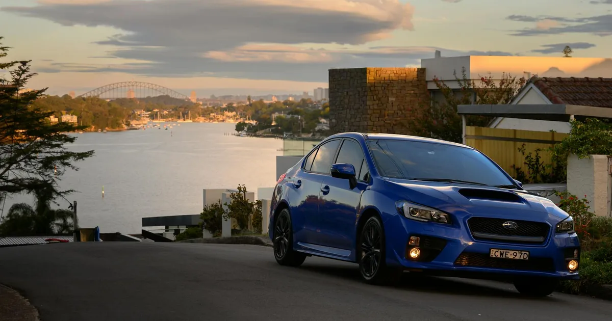 Blue car parked on a road overlooking a waterfront with distant.