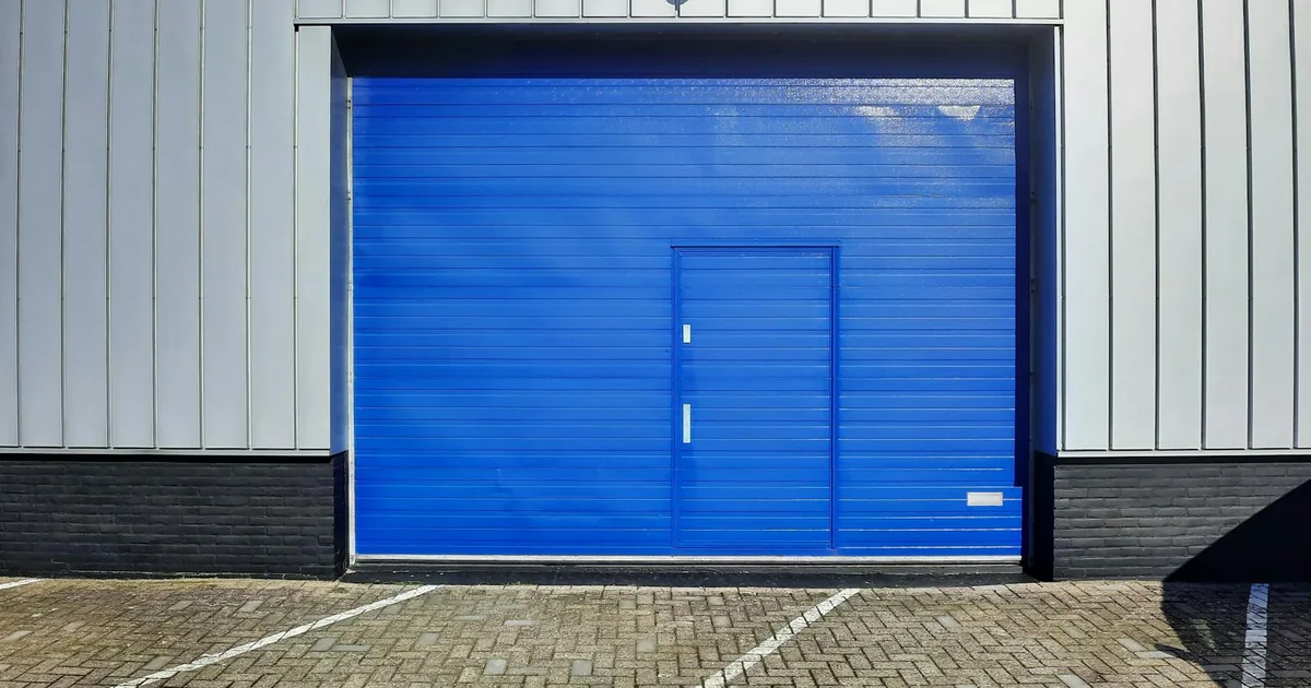Blue garage door with a small side door in a parking lot setting.