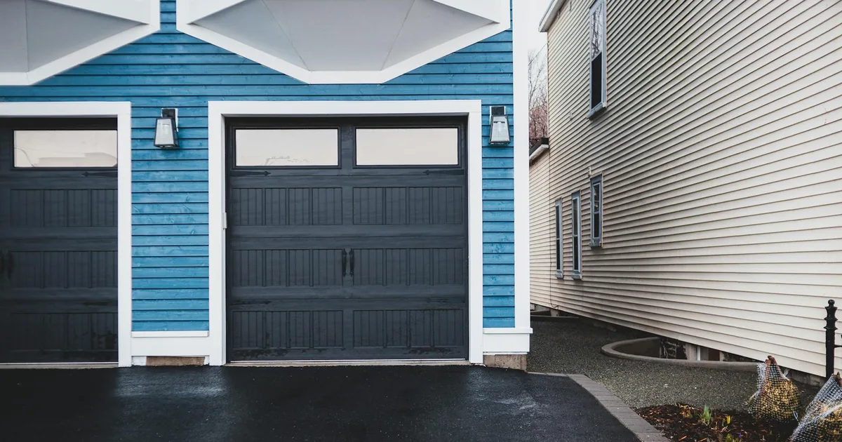 Blue house with a garage door next to a narrow pathway and another.
