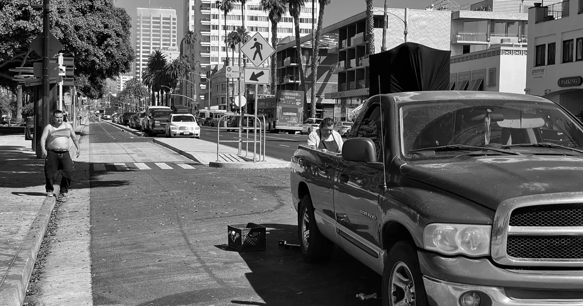 Busy street with parked vehicles and pedestrians walking by.