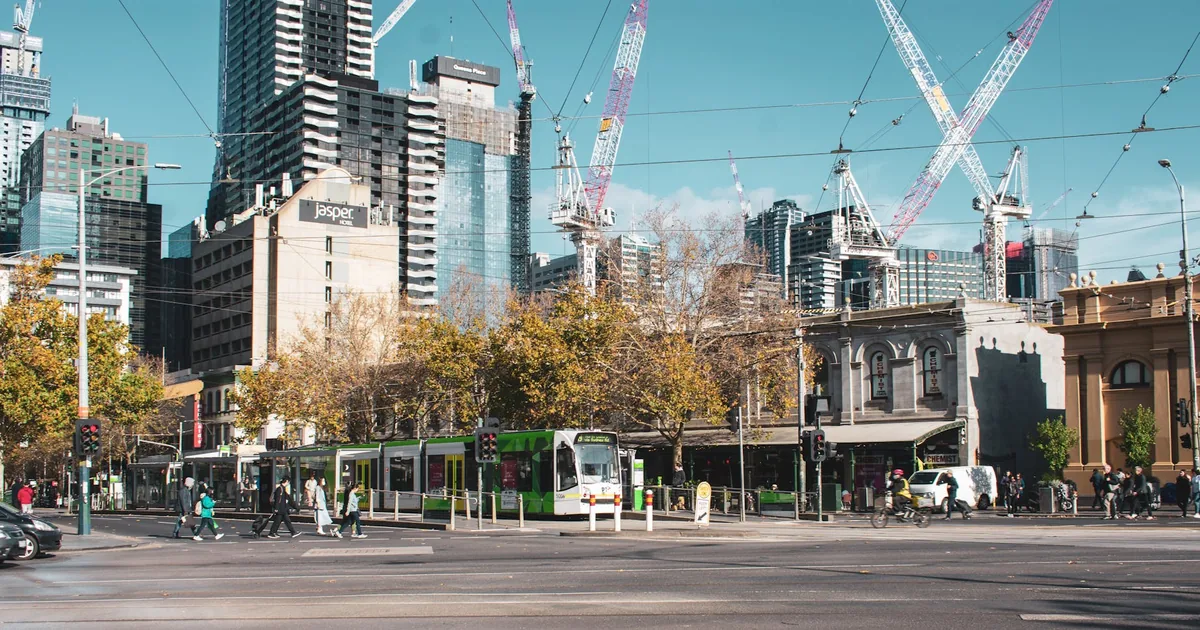 Busy urban street with parked cars trams and pedestrians near tall.
