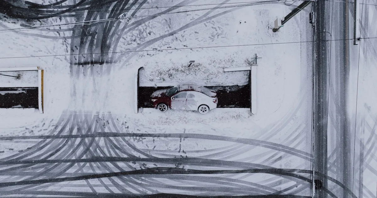 Car parked in a snowy area with tire tracks visible around it.