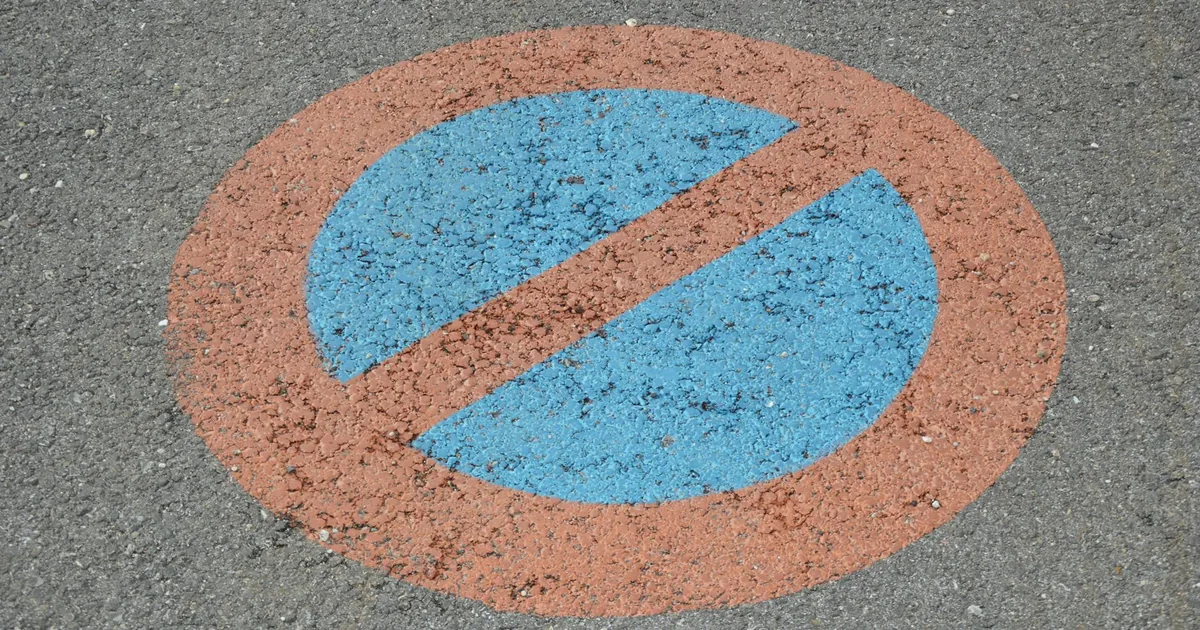 Circular no parking sign painted on a gray asphalt surface.