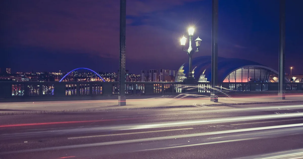 City parking area at night with streetlights and blurred car lights.