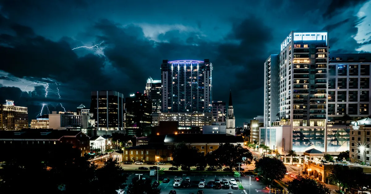 City parking lot illuminated at night with buildings and stormy.