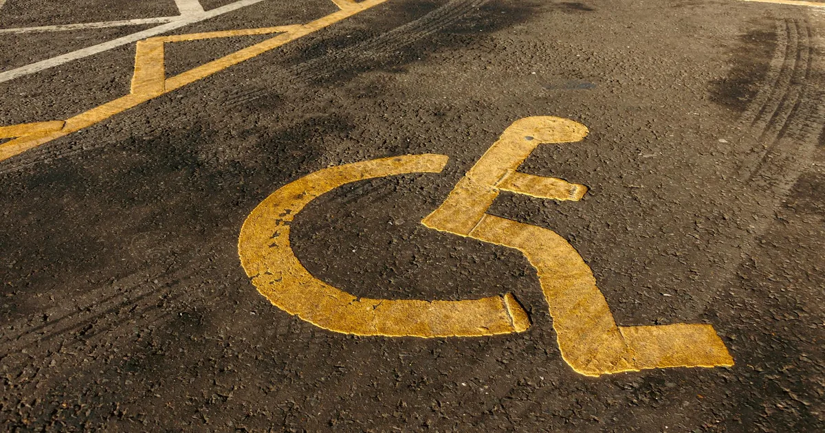 Close up of a faded yellow handicap symbol on a parking lot surface.