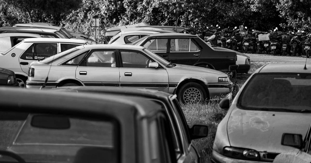Crowded parking area with various cars and motorcycles visible.