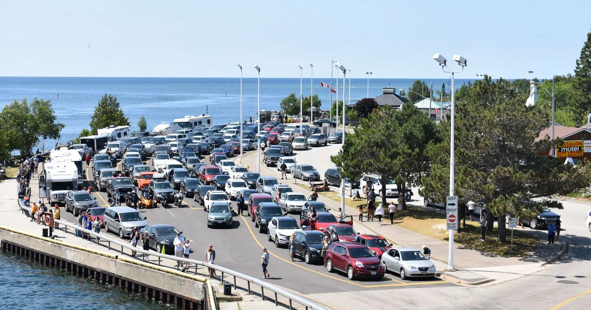Crowded parking lot near the water with various vehicles and trees.