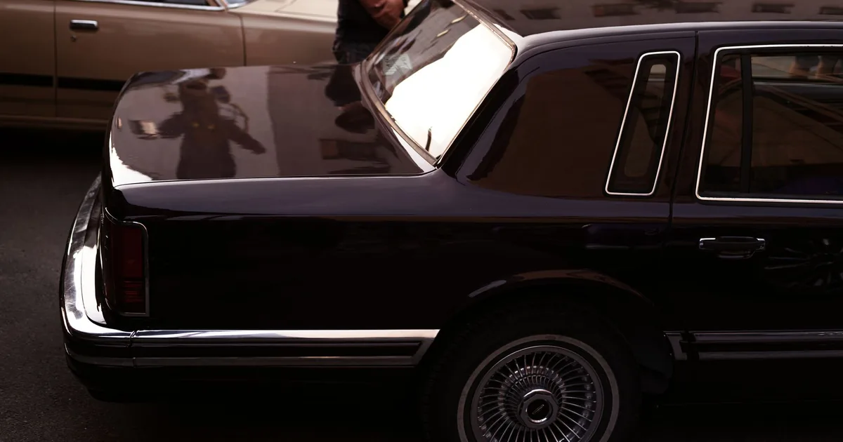 Dark car parked beside a light colored vehicle in a parking area.