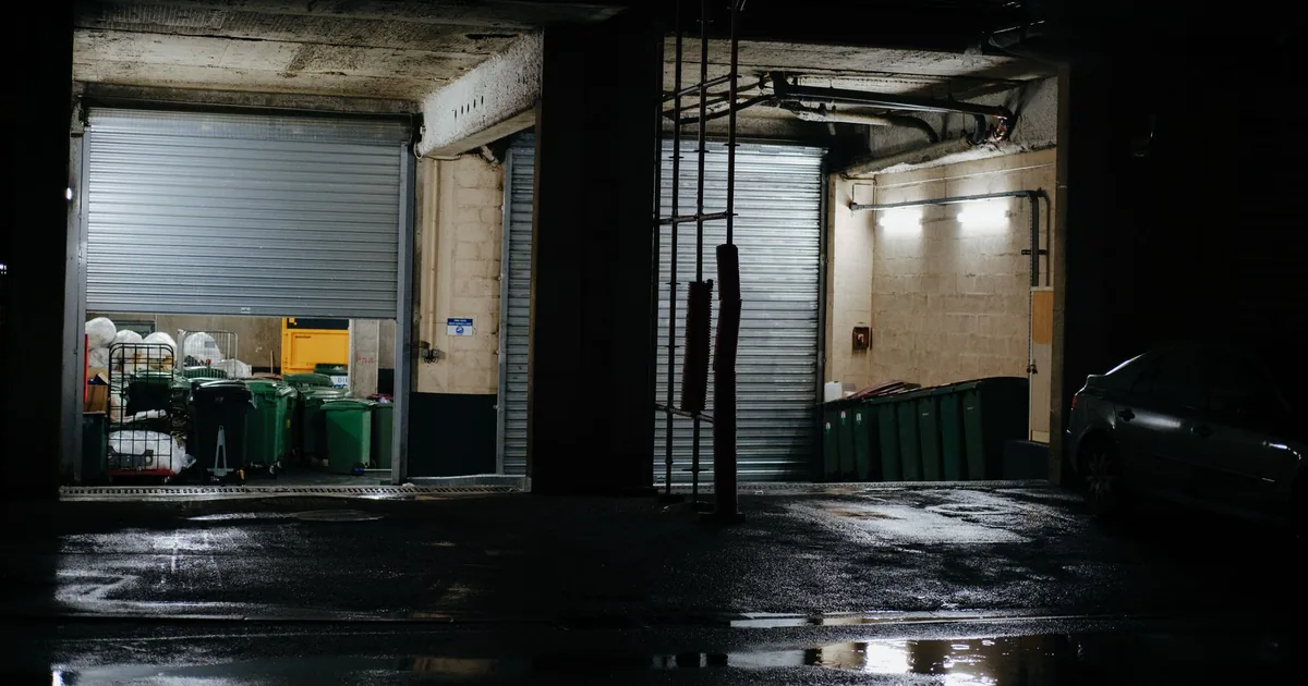 Dimly lit parking garage with metal roll up doors and green waste.