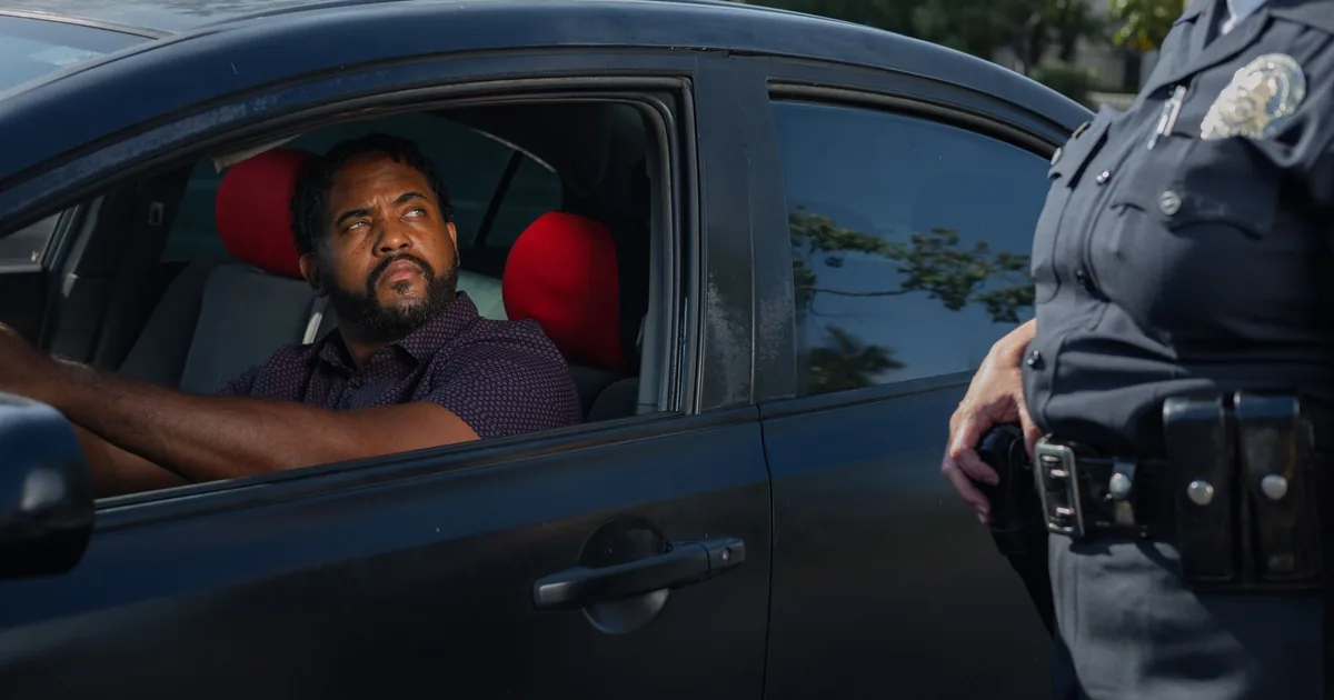 Driver in a parked car looks at a police officer nearby.