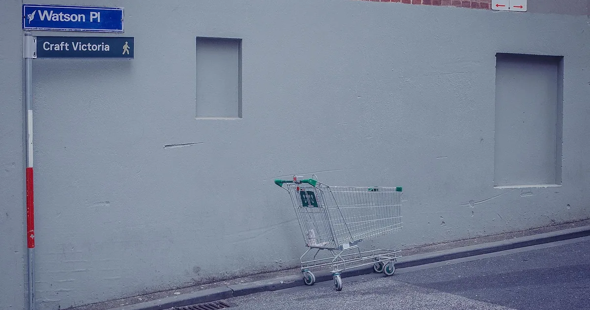 Empty shopping cart is parked beside a gray wall in a parking area.
