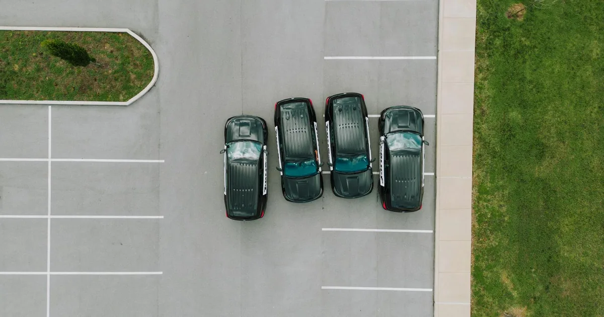 Four cars parked in a row on a gray asphalt parking lot with green.