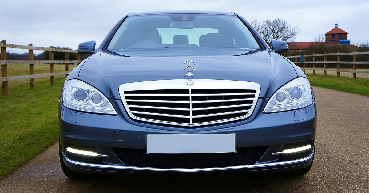 Front view of a parked car on a gravel driveway near a wooden fence.
