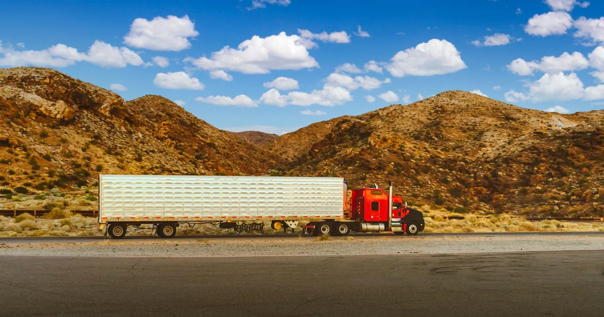 Large truck parked beside a road with mountains and blue sky in the.