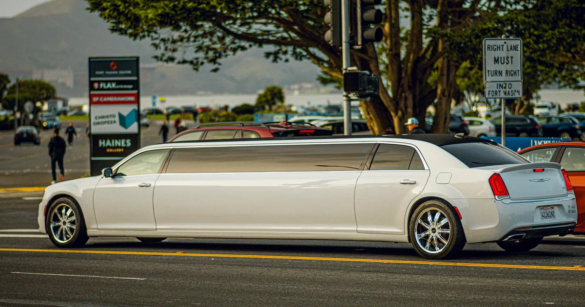 Long white limousine parked on a city street near traffic lights.