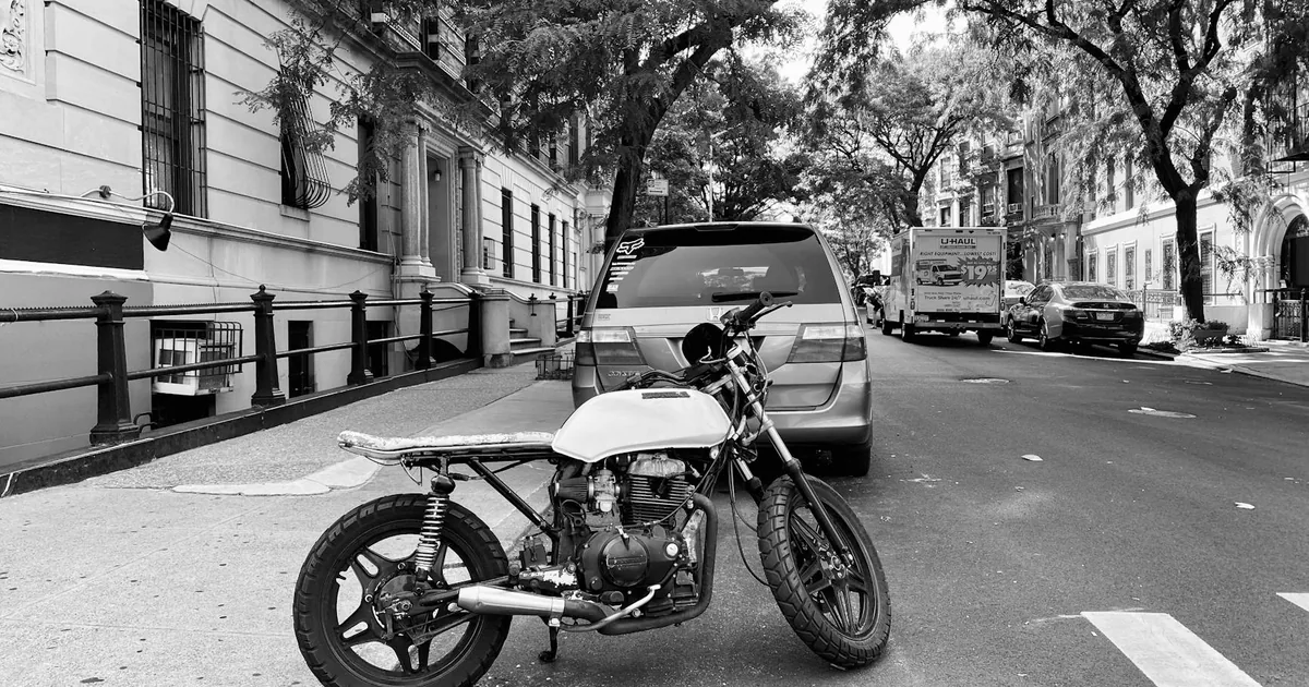 Motorcycle and a van parked on a tree lined street.