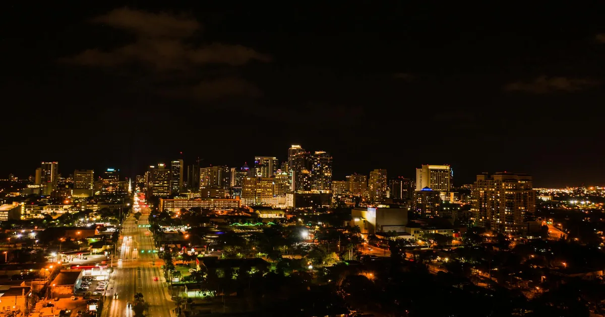 Nighttime city skyline with illuminated buildings and empty parking.