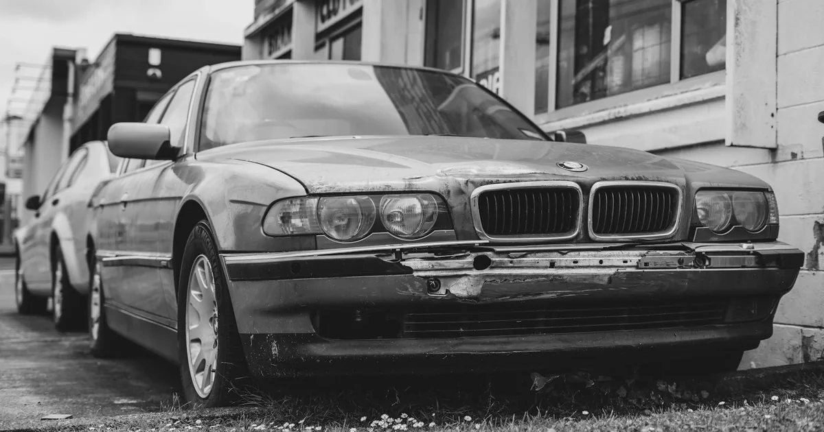 Old parked car with visible wear and tear in a parking space.