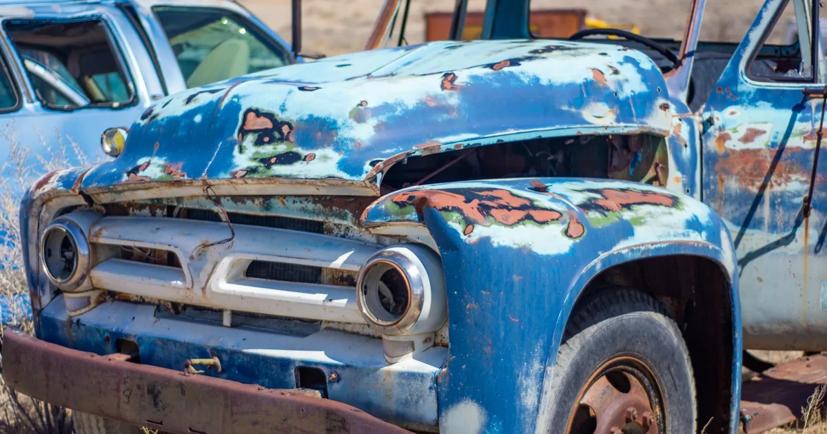 Old rusty vehicles parked in a dusty lot with peeling paint and.