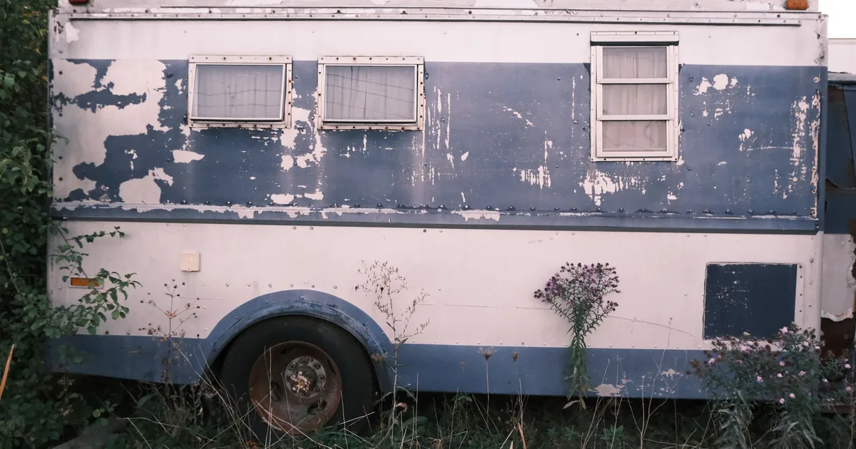 Old weathered trailer with peeling paint parked in a grassy area.