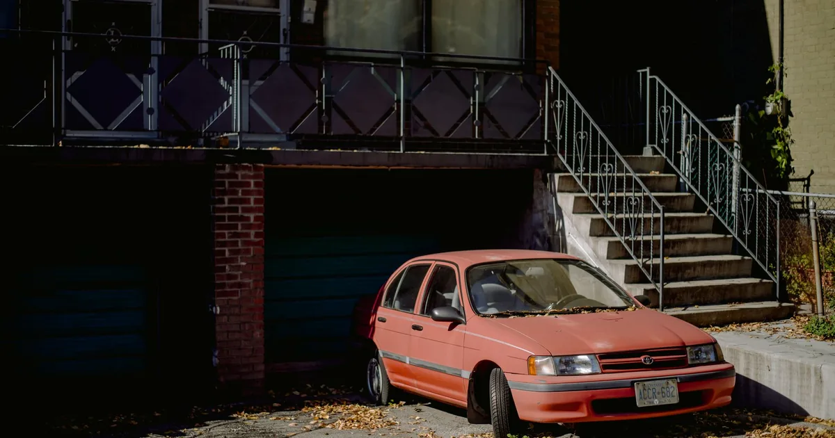 Parked car beside a building with stairs and leaves on the ground.