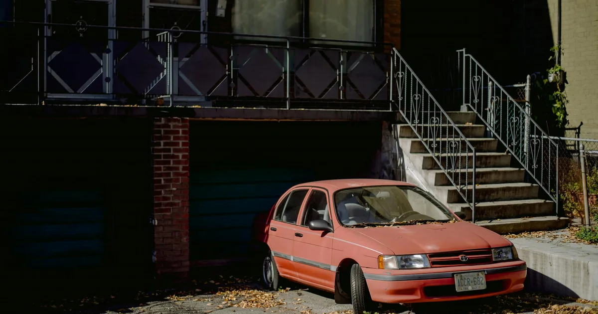 Parked car beside a building with stairs and leaves scattered on.