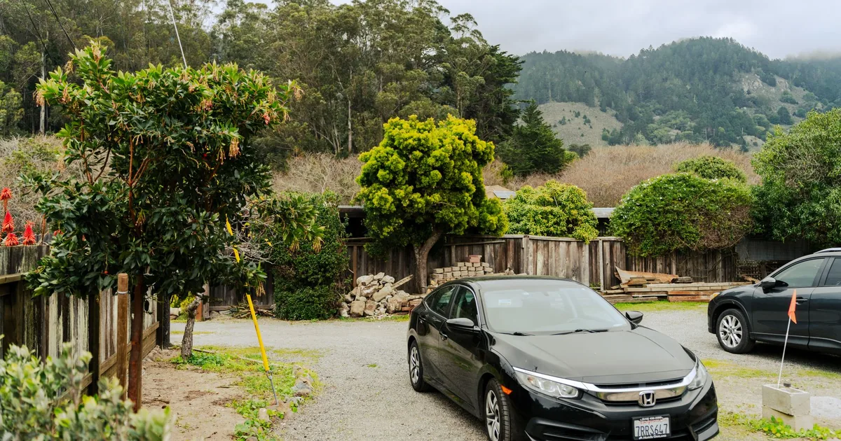 Parked car in a gravel lot surrounded by trees and shrubs.