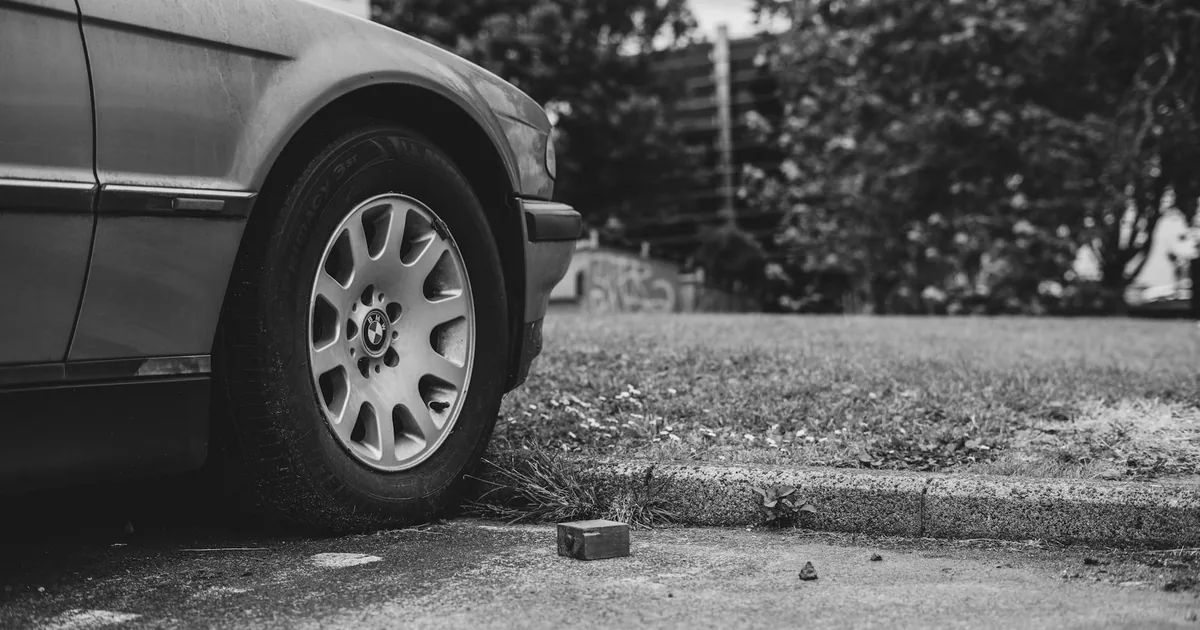 Parked car with a close up of its wheel next to a grassy area and.