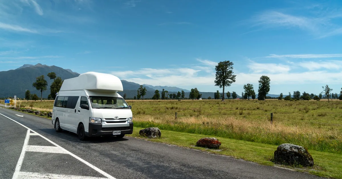 Parked van beside a grassy area with mountains in the background.