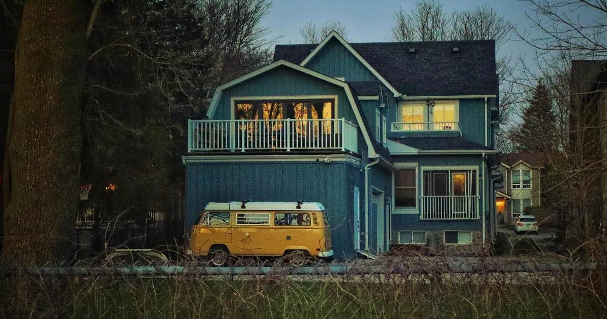 Parked vehicle beside a blue house with a balcony in a quiet.