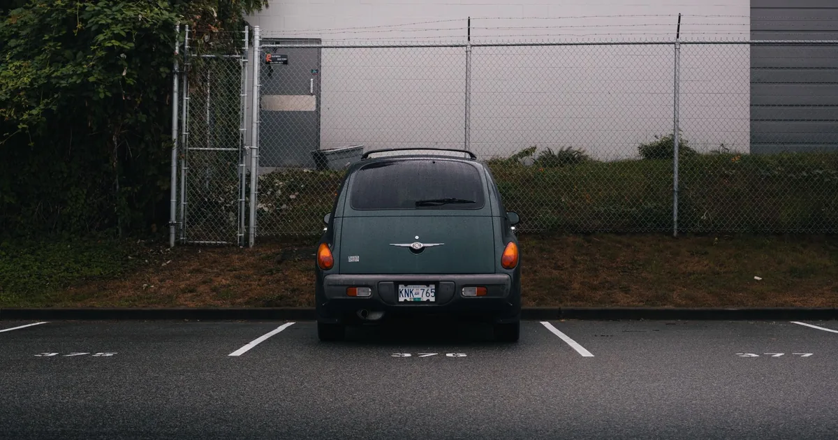 Parked vehicle in a parking lot with a fence and building in the.