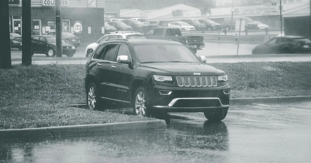 Parked vehicle in the rain surrounded by wet pavement and grassy.