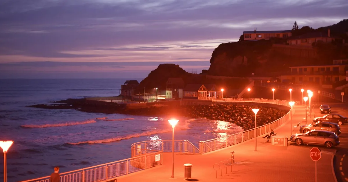 Parking area along the coast with cars and ocean view at sunset.