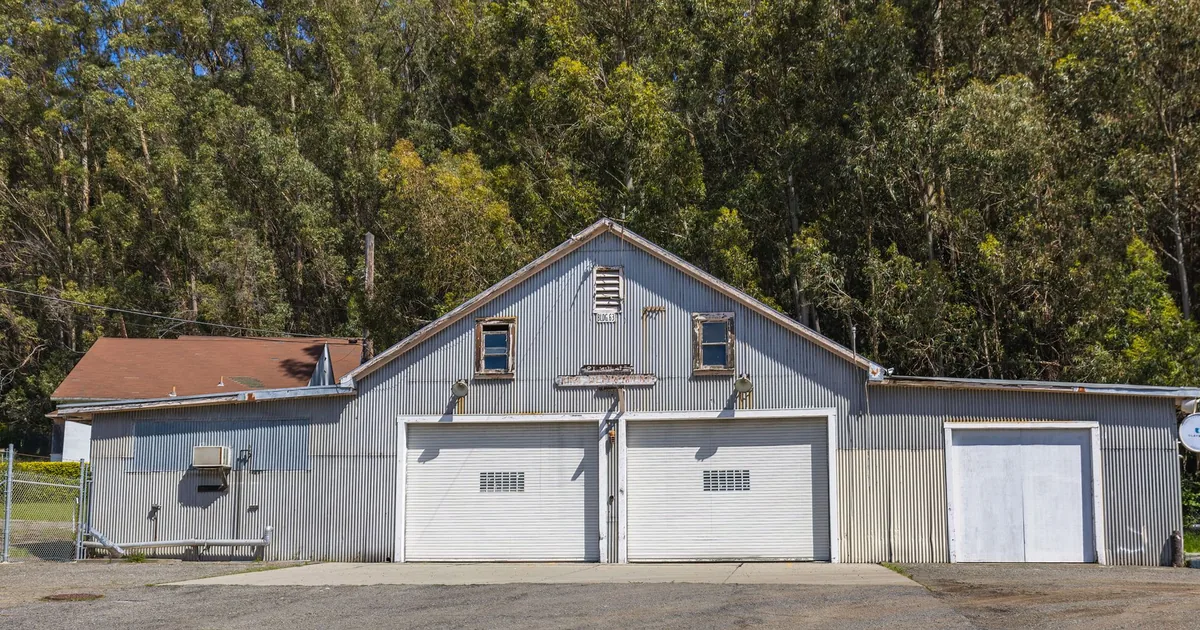 Parking area in front of a building with two garage doors and trees.